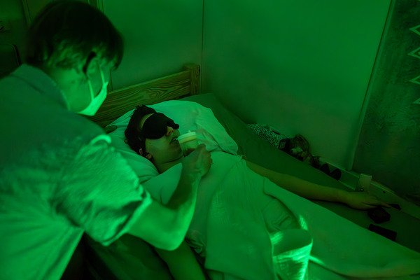 AUSTRIA, AUGUST 2024: AUSTRIA, AUGUST 2024: Mila's father Joachim gives his severely ill daughter liquid food and water in a dark room while using only a tiny green light.  He puts moisturizer on her lips to prevent them from cracking. Mila's parents