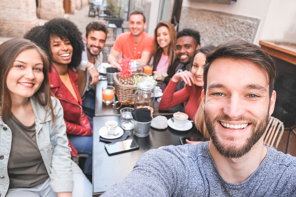 Group of happy friends drinking coffee and cappuccino at bar outdoor - Young millennials people taking selfie while doing breakfast - Friendship, youth and food concept - Focus on right man face